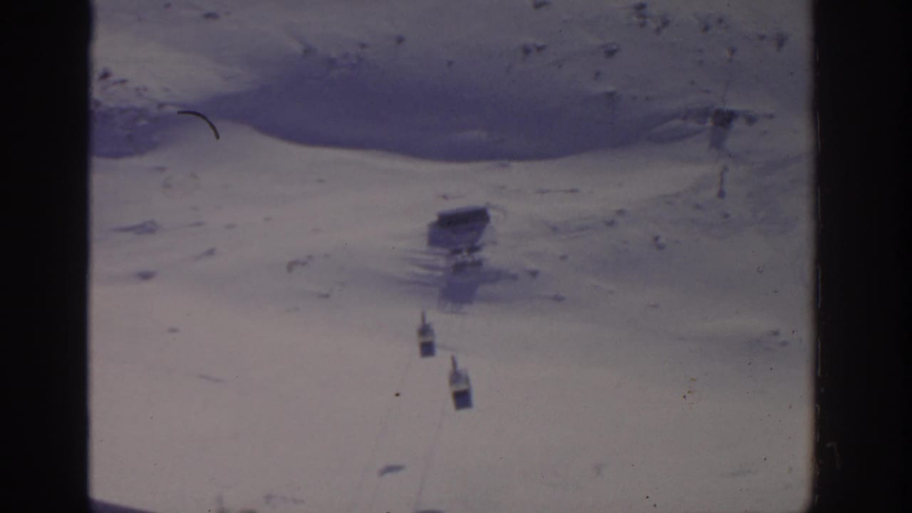 Cable car cabins appear below a small structure or support on a snowy mountain slope.