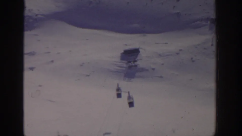Vintage 8mm frame from the Munich winter tram footage, showing two cabins over snow with soft focus and faded color.