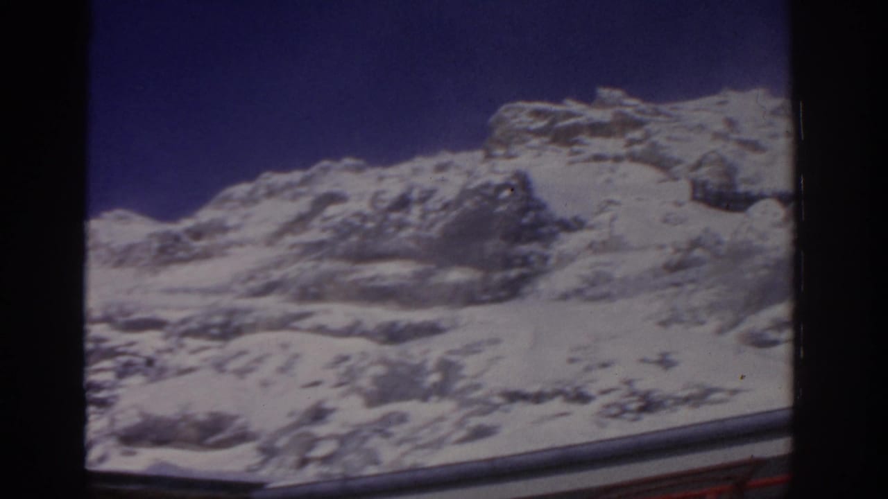 Snow-covered rocky mountain slope beneath a deep blue sky, with dark film borders.