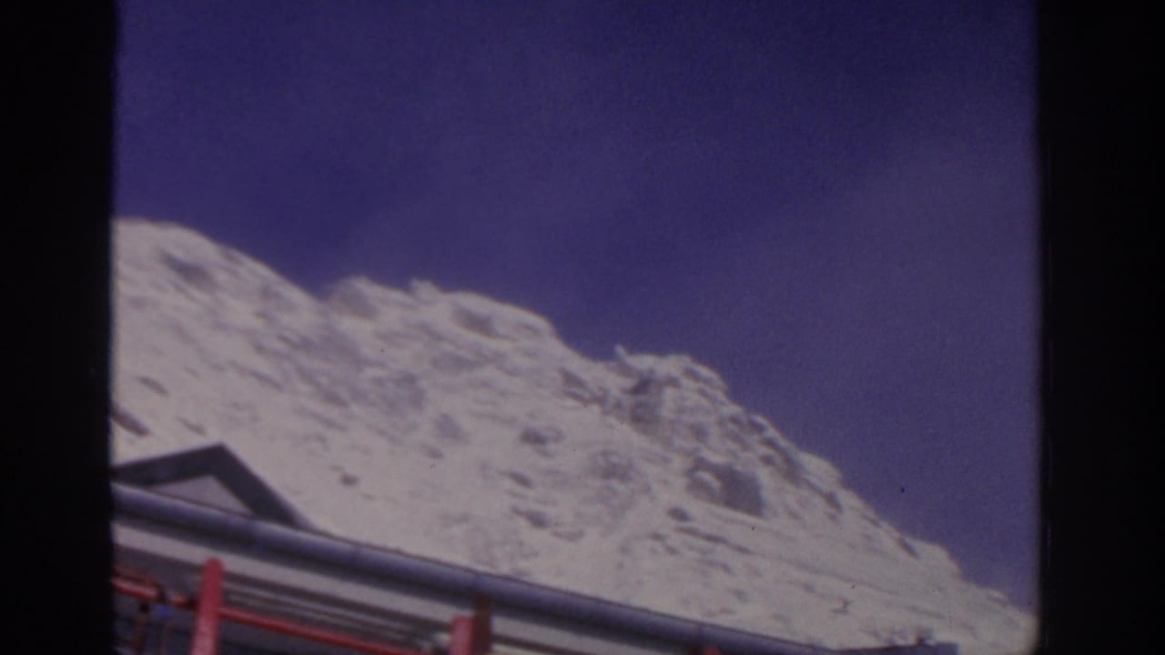 Snowy mountain slope under a dark blue-purple sky with a bus roof edge in the foreground.