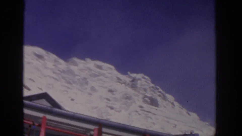 1963 8mm travel frame near Munich showing a snow-covered mountain above the red and silver top edge of a bus.