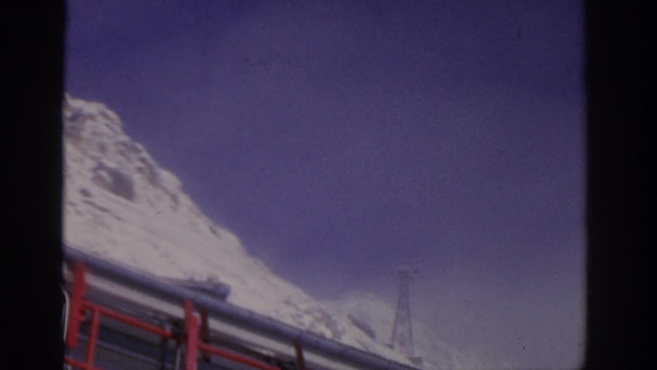 Snowy peak and bus roof with red railings beneath a clear dark sky.