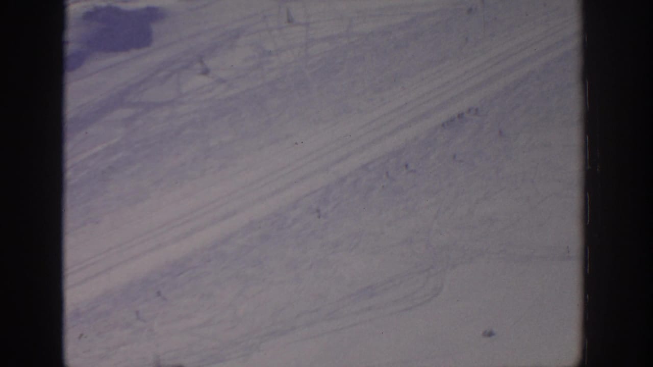 1963 8mm aerial view from the Munich metadata, showing pale desert-like ground with subtle tracks and cool color shift.