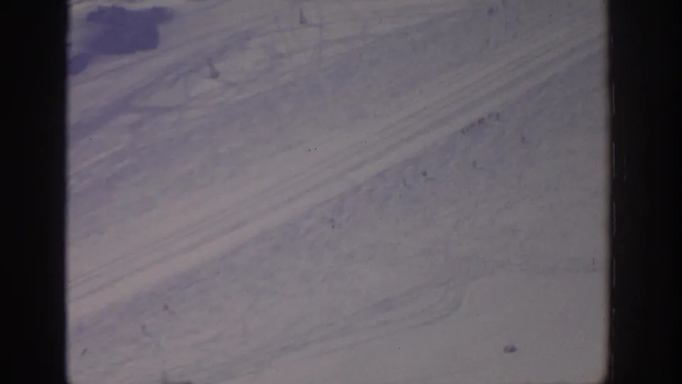 1963 8mm aerial view from the Munich metadata, showing pale desert-like ground with subtle tracks and cool color shift.
