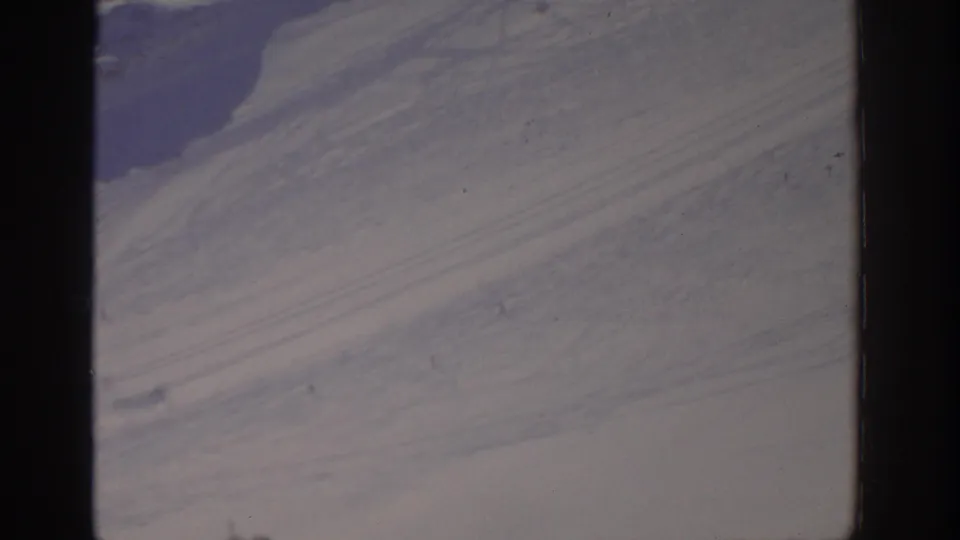 1963 aerial home-movie frame showing a pale, barren-looking surface with faint tracks and a darker patch along the left edge.