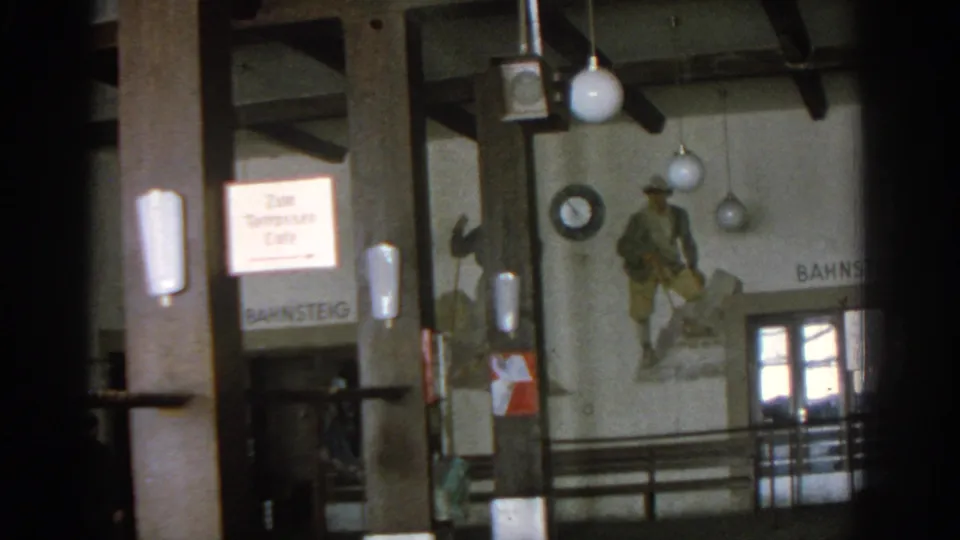 1963 Munich station-side interior with a partially visible cafe sign, Bahnsteig 1 text, wall mural, globe lights, and doors.