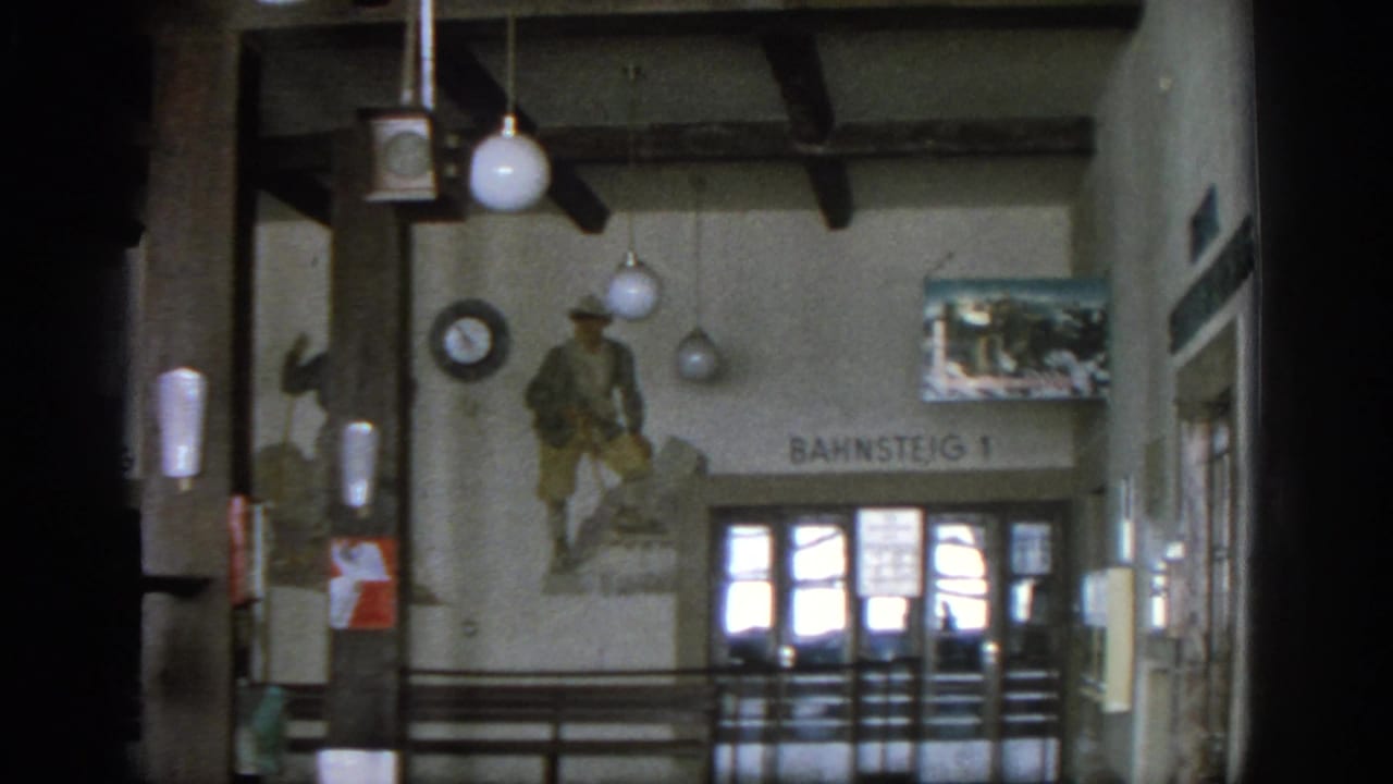 1963 Munich station interior showing a Bahnsteig 1 sign, soldier mural, globe lights, wall clock, railings, and glass doors.