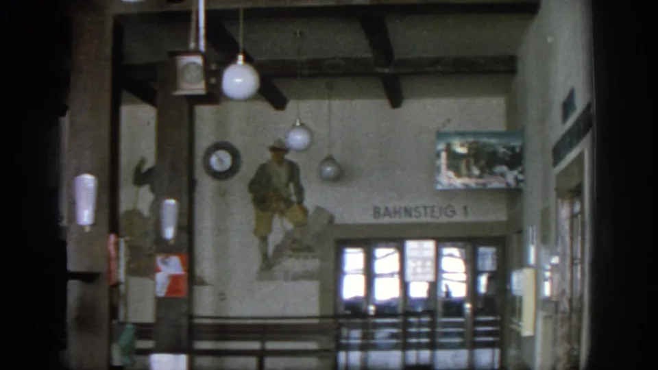 1963 Munich station interior showing a Bahnsteig 1 sign, soldier mural, globe lights, wall clock, railings, and glass doors.