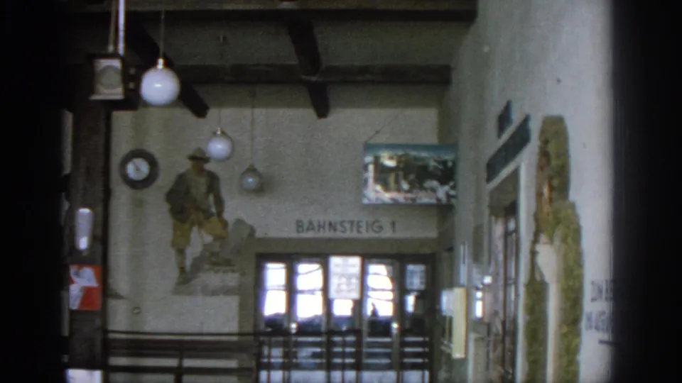 1963 Munich station view with soldier mural above the Bahnsteig 1 entrance, hanging lights, clock, glass doors, and wall artwork.