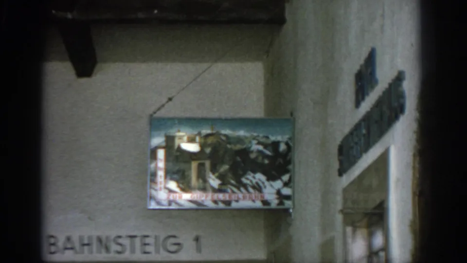 Soft 8mm view of a painted mountain sign and cropped Bahnsteig 1 text inside the reported Munich hotel setting.