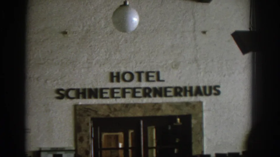 Visitor-shot 1963 frame showing the Hotel Schneefernerhaus sign, globe light, and recessed entrance on a German hotel facade.