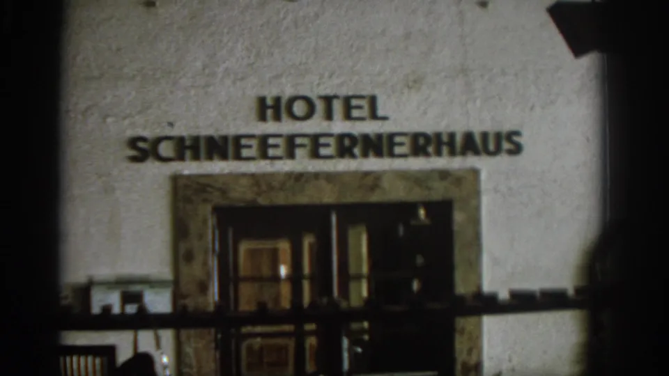 1963 8mm frame of Hotel Schneefernerhaus, with the name, stone-framed doors, railing, and soft home-movie focus visible.