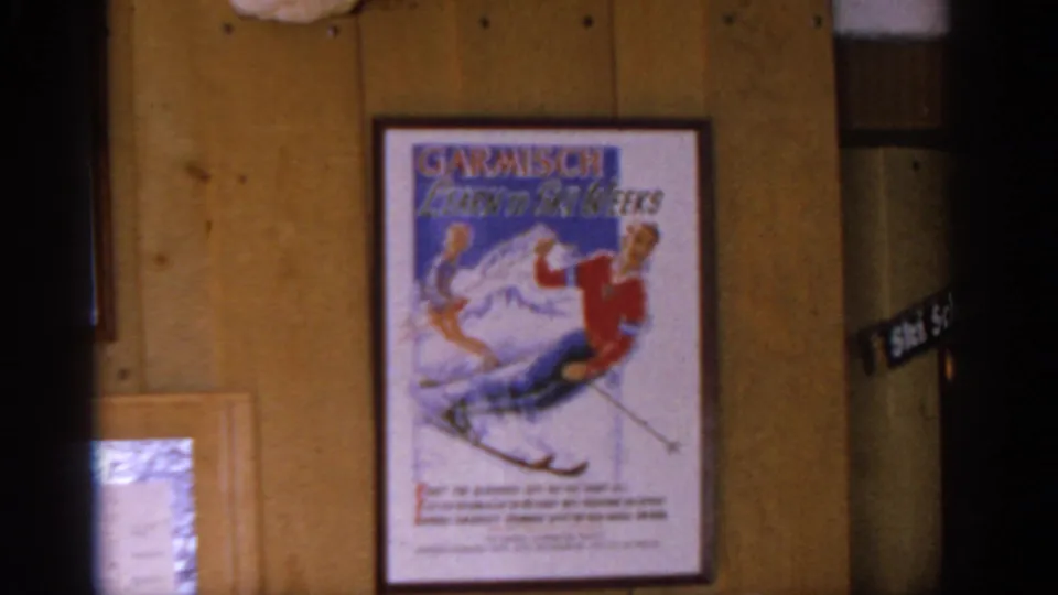 A framed Garmisch Learn to Ski Weeks poster hangs on a wood-paneled wall, reinforcing the alpine travel setting.