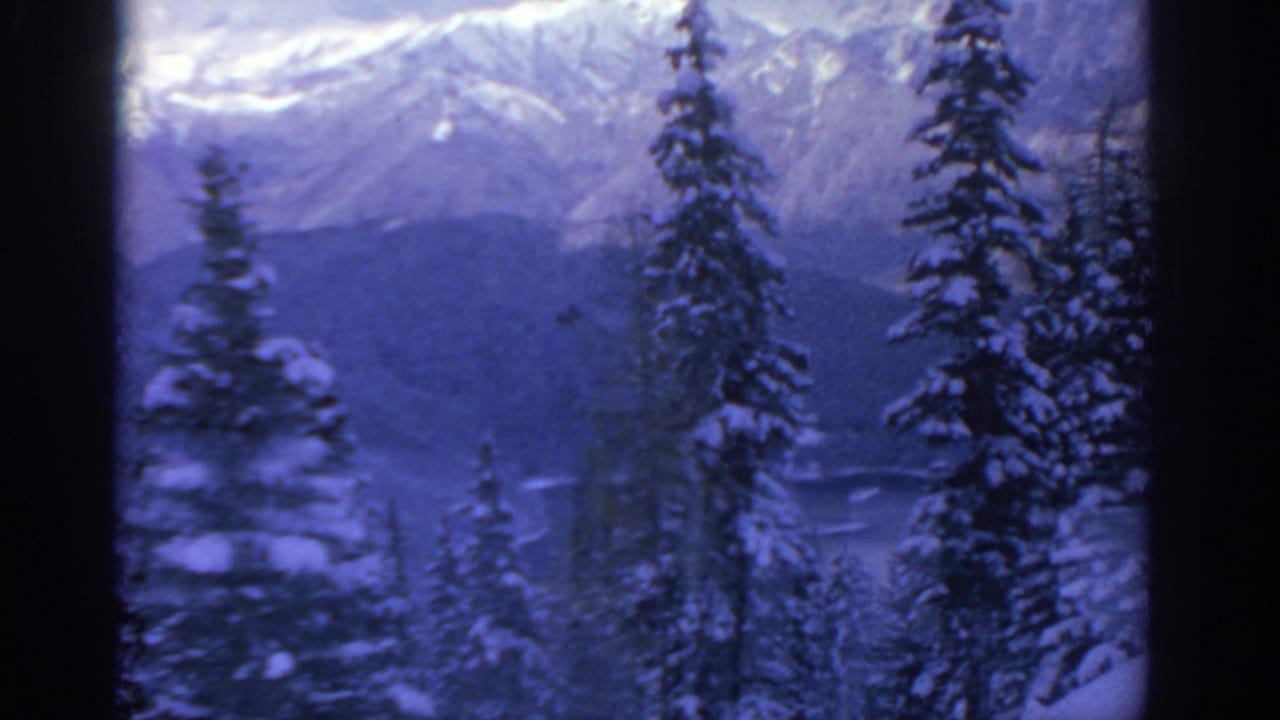 1963 8mm home-movie frame from the Munich-area clip showing snow-laden evergreens and distant mountain ridges.
