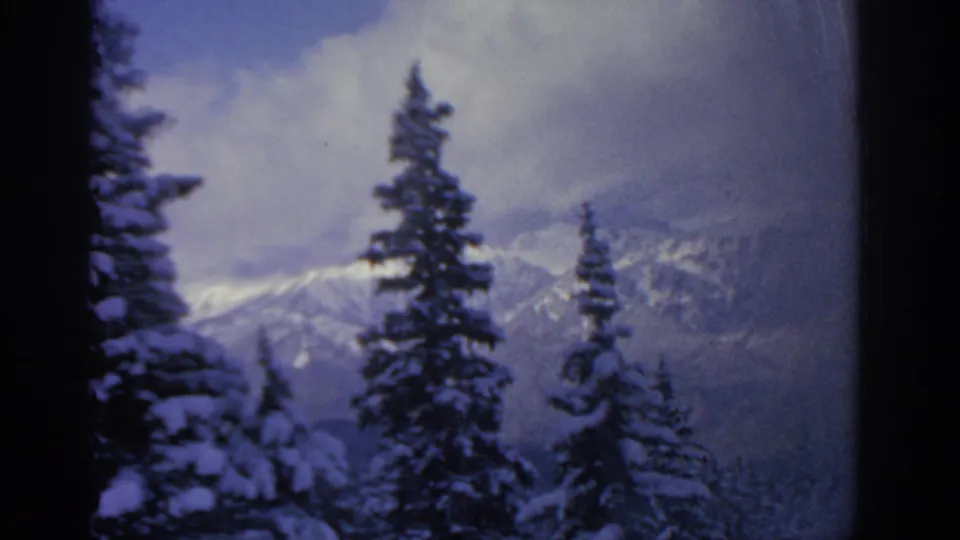 Cool-toned 8mm frame from the 1963 Munich-area clip, with snowy pines and hazy mountain ridges in view.