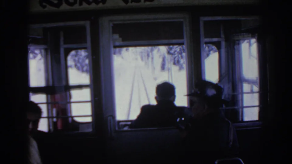 1963 home-movie frame from inside a train or rail car, with silhouetted passengers facing bright winter scenery outside.