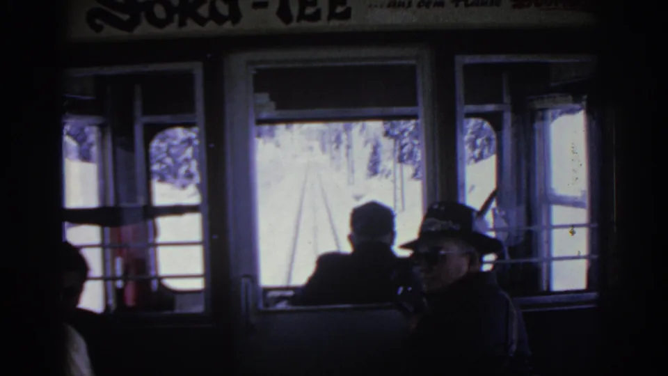 1963 Munich-area travel footage showing passengers inside a rail car, including a hatted adult near the windowed winter view.