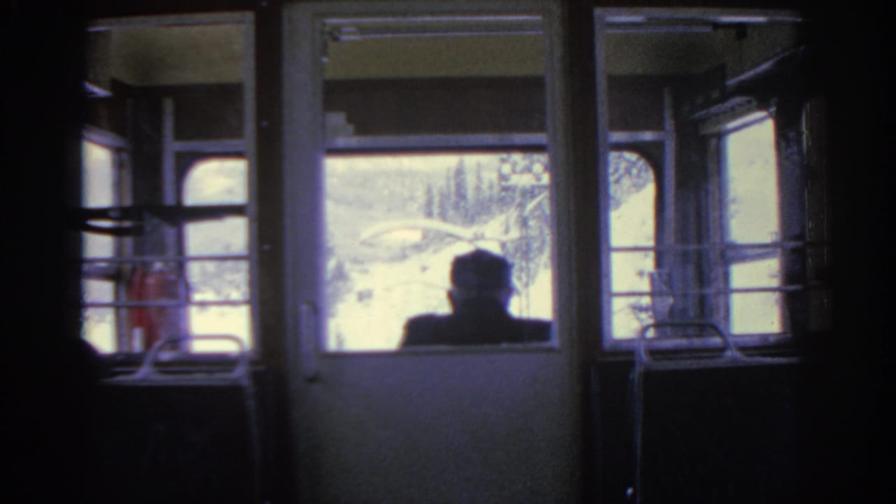 1963 Munich train interior with a passenger silhouette seated before bright snowy windows and carriage fixtures.