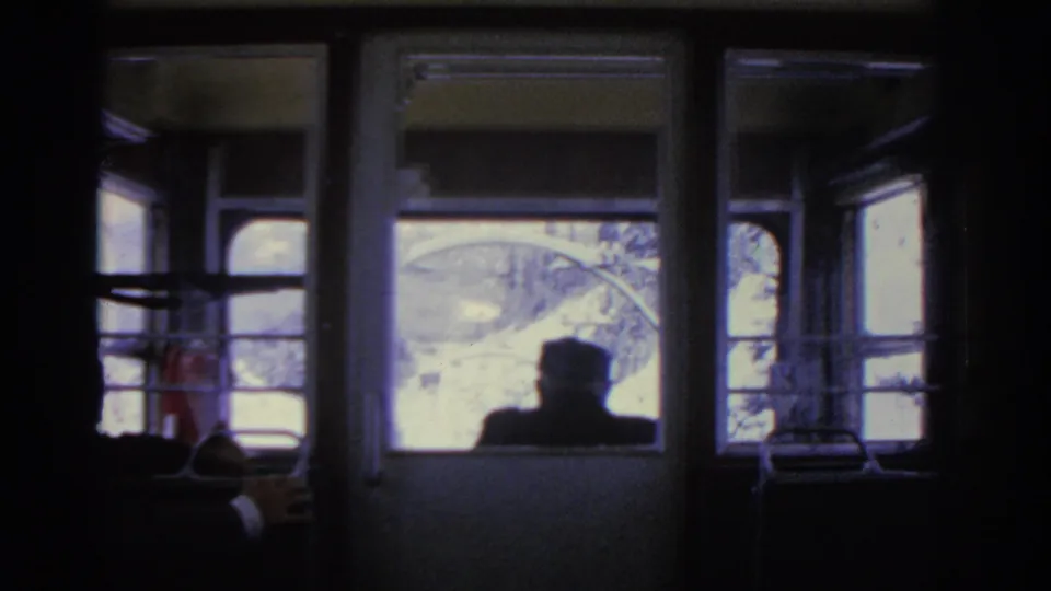 A dark 1963 Munich train interior frames a passenger silhouette and a snowy landscape seen through multiple windows.