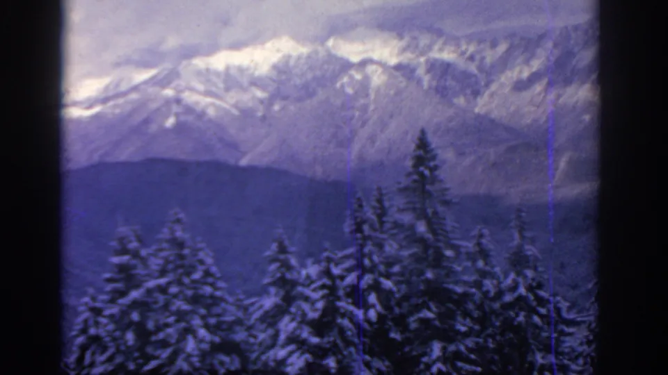 Snow-covered trees and a distant mountain range appear in a soft, blue-purple 8mm travel frame from the 1963 clip.