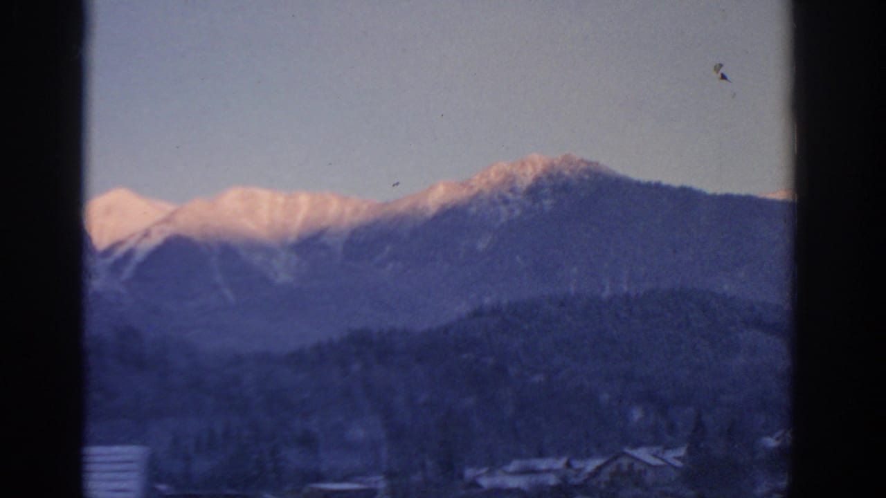 Snowy mountain ridge and village roofs seen through dark vertical framing.