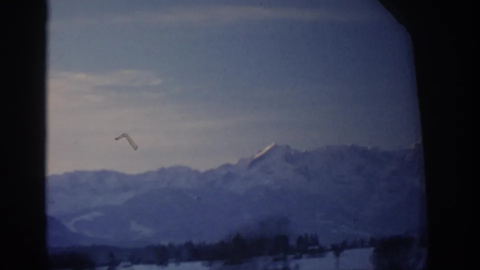 1963 8mm Munich-area travel frame with blue-tinted snowy mountain ridges, treeline, and visible film texture.