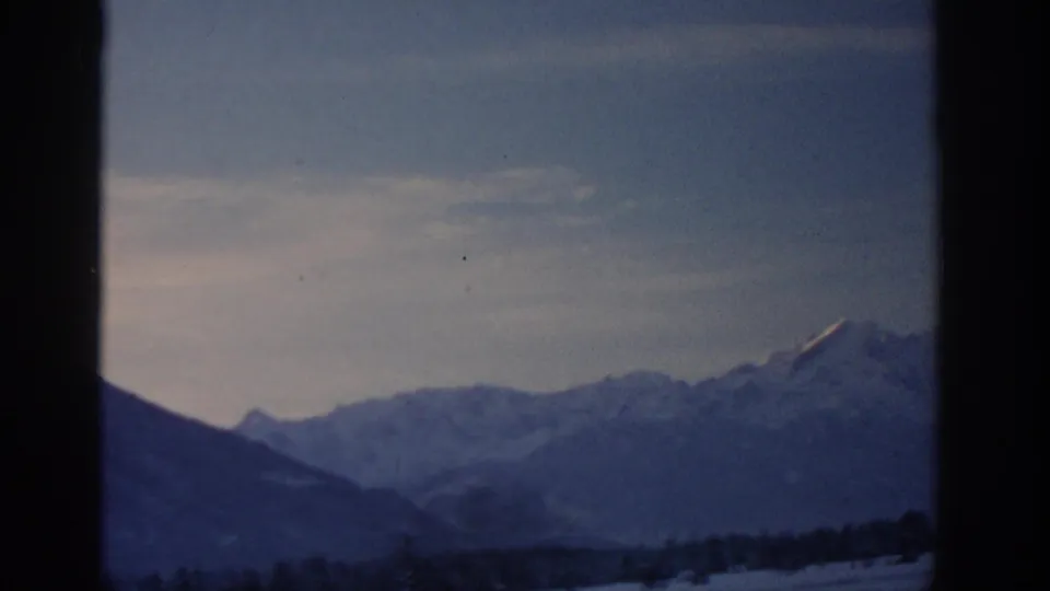 Snowy Alpine ridge in a 1963 8mm home-movie frame attributed to the Munich area, with muted blue winter tones.