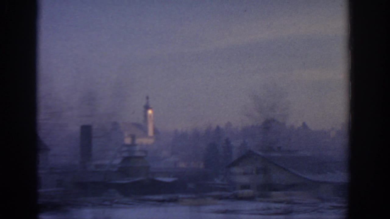 Hazy exterior view through a window with distant buildings and a lighted tower.