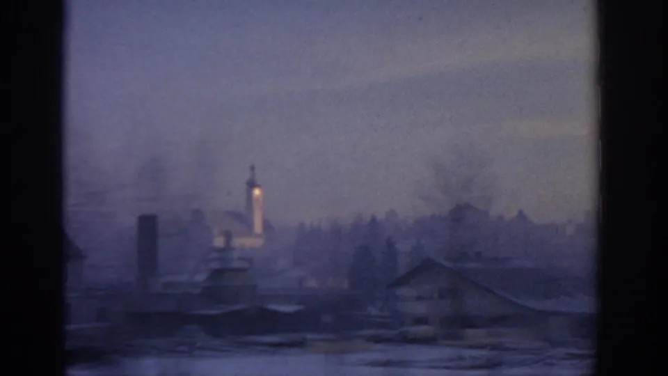 Soft 1963 Munich view through station glass, showing a hazy exterior skyline and a small illuminated tower beyond the windows.