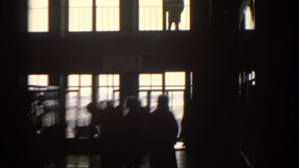 1963 Munich transit interior with travelers in silhouette below bright window panels and a single figure visible on the upper level.