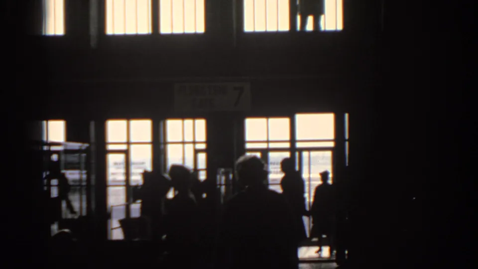 Silhouetted travelers stand near bright glass doors in a Munich transit hub, with a partially readable FLUGSTEIG GATE 7 sign above.