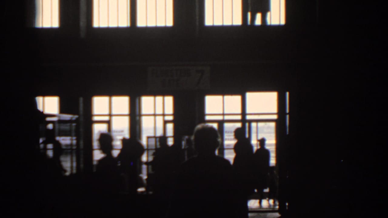 Silhouetted travelers stand and walk inside a dim airport terminal beneath bright windows.