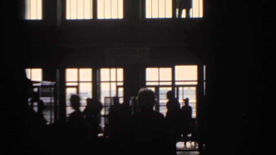 Silhouetted travelers move through a dim Munich airport gate area in 1963, with bright windows and a Flugsteig 7 sign visible above.
