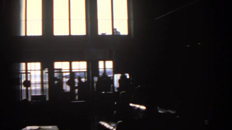 Backlit figures appear near a Munich airport gate in 1963, with window grids and terminal fixtures visible in deep shadow.