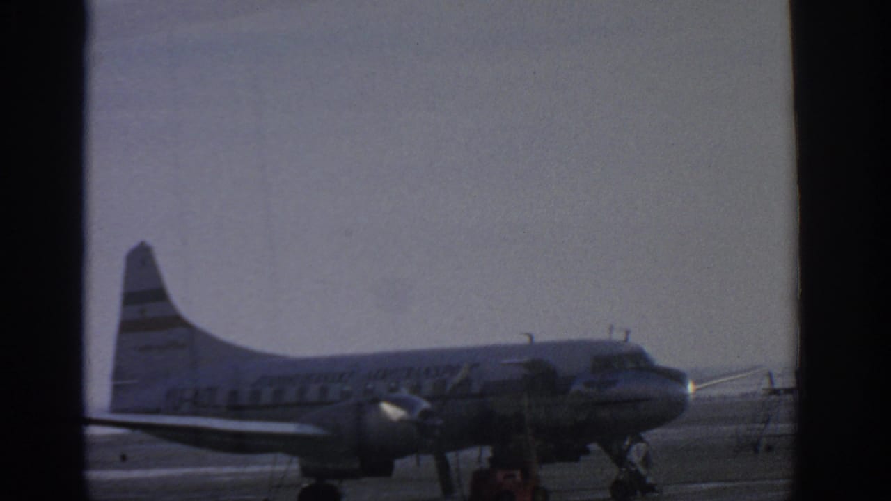 Propeller airplane on tarmac with stairs and service equipment nearby.