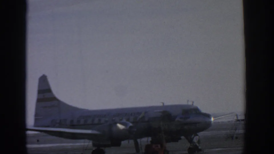 A 1963 Munich tarmac shot shows a propeller passenger aircraft with a striped tail, service stairs, and small ground equipment nearby.