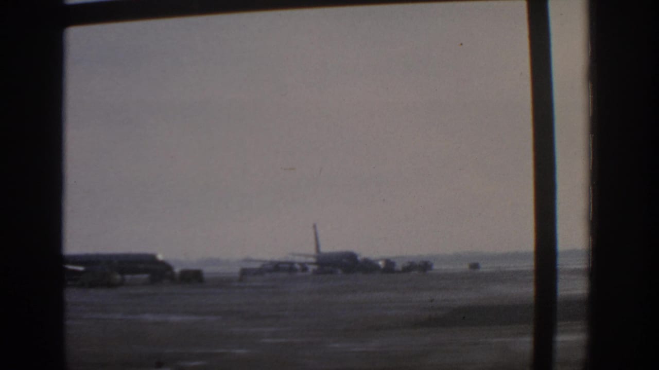 Distant aircraft and ground vehicles on a tarmac behind a large window.
