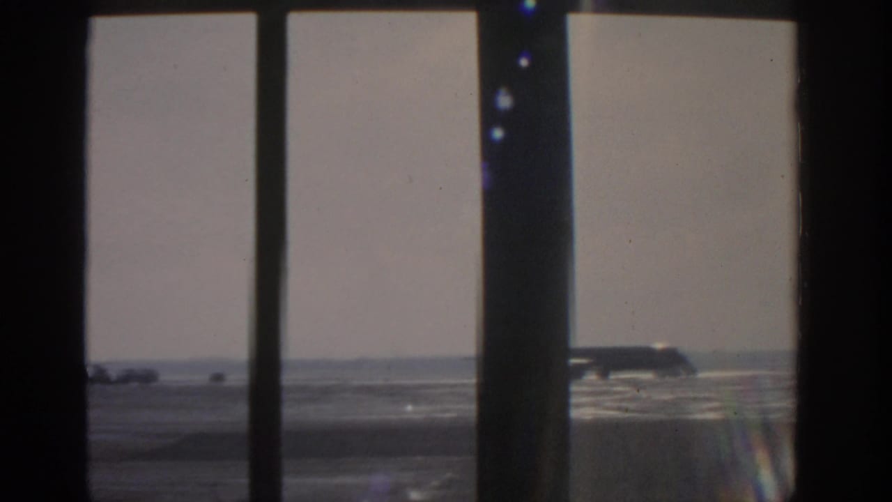 Parked silver airplane seen through dark window frames at an airfield.
