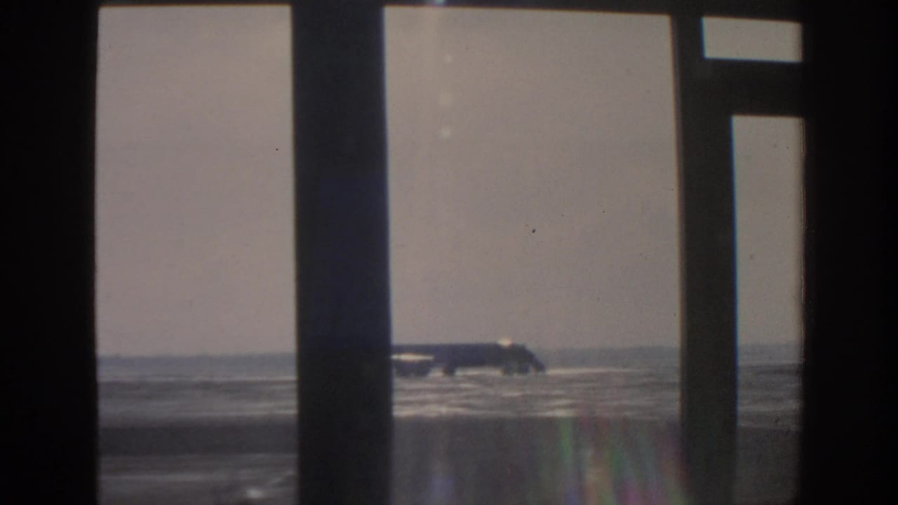 Silver airplane on the tarmac framed by vertical window supports.