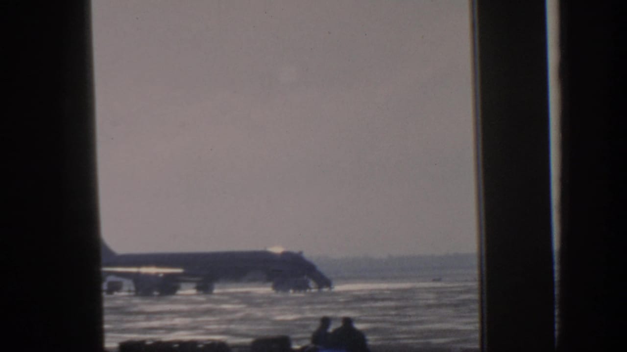 Distant airplane on a wet tarmac seen through dark window framing.