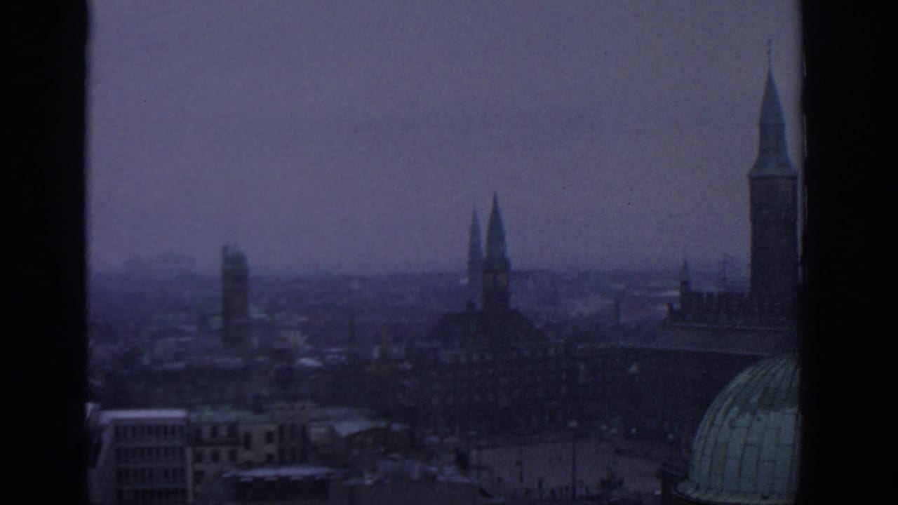 Hazy city skyline with church spires seen through vertical window bars.