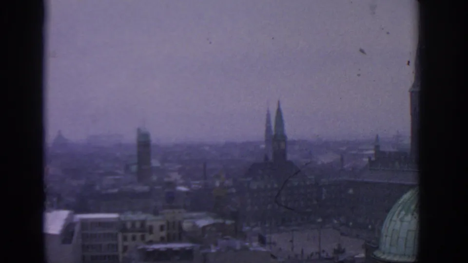 1963 8mm view over Warsaw, Poland, showing distant spires, dense rooftops, haze, and a green dome framed by dark borders.