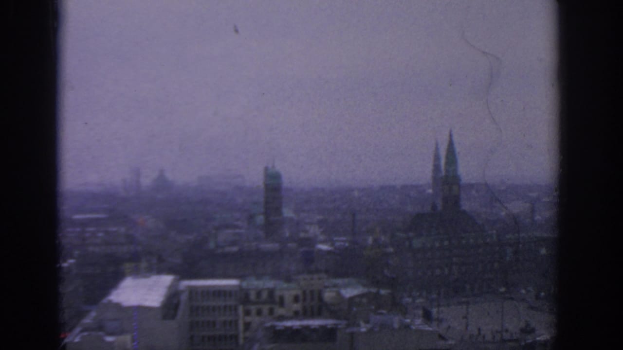 Soft, hazy city skyline with twin spires at right and rooftops below.