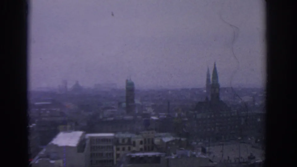 Elevated 1963 Warsaw city view with twin spires at right, low rooftops below, and muted purple-gray sky haze.
