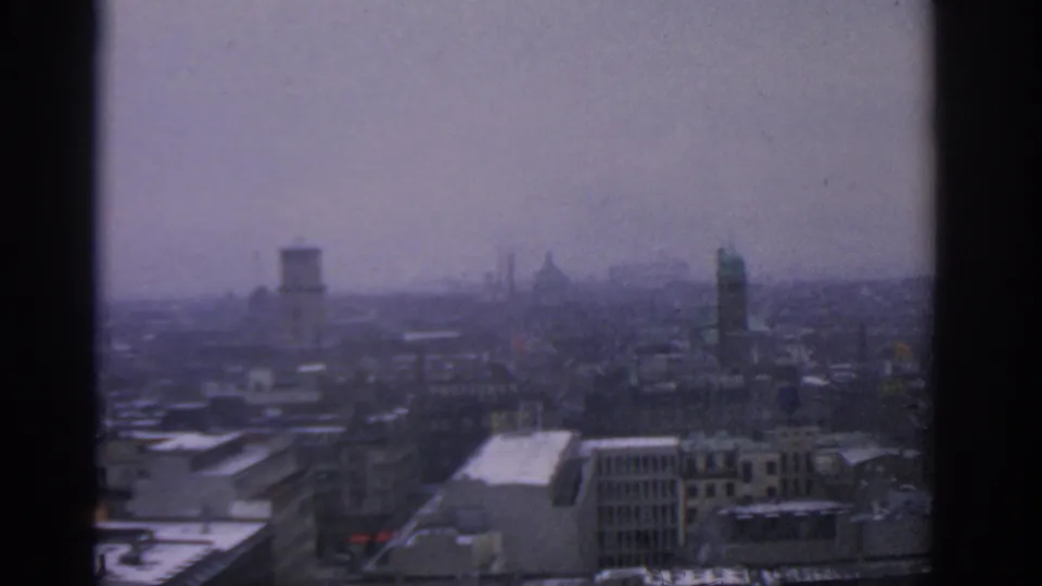 Late-frame 1963 Warsaw city view showing rooftops, distant tower shapes, urban haze, and muted 8mm color.