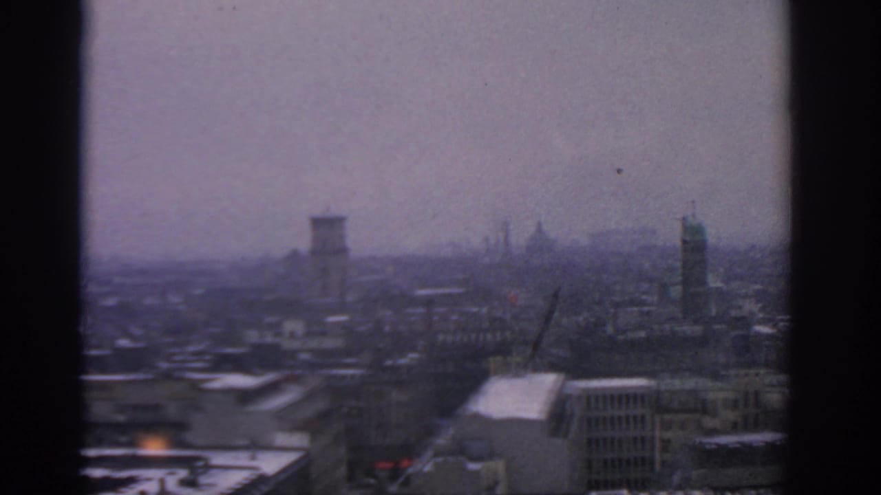 Hazy city rooftops and towers seen from a high vantage point.
