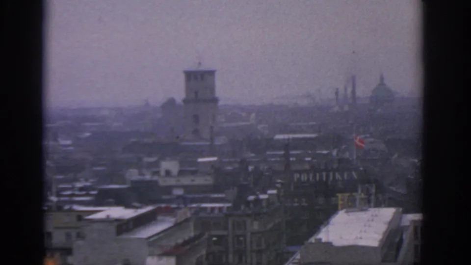 End frame of the 1963 Warsaw city view, with a tower near center, distant domes or spires, snowy roofs, and dark window borders.