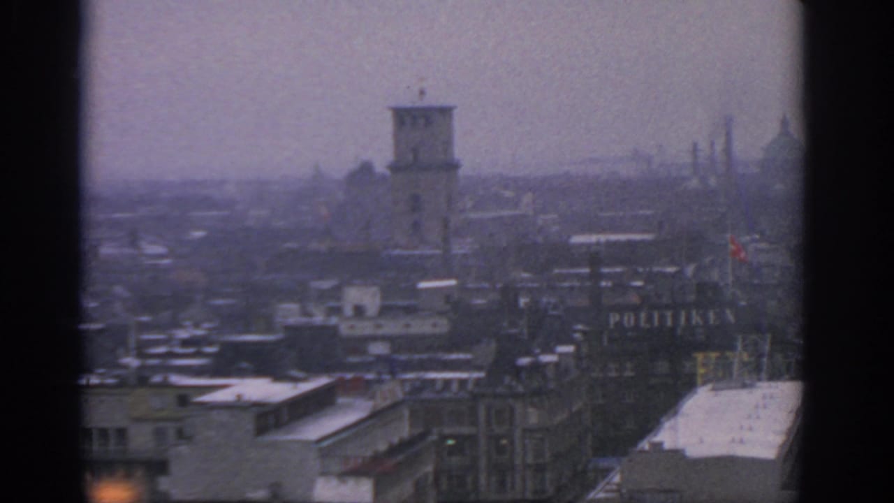 1963 Warsaw view across snow-dusted rooftops toward a tower, distant spires, and a partly visible POLITIKEN sign in haze.
