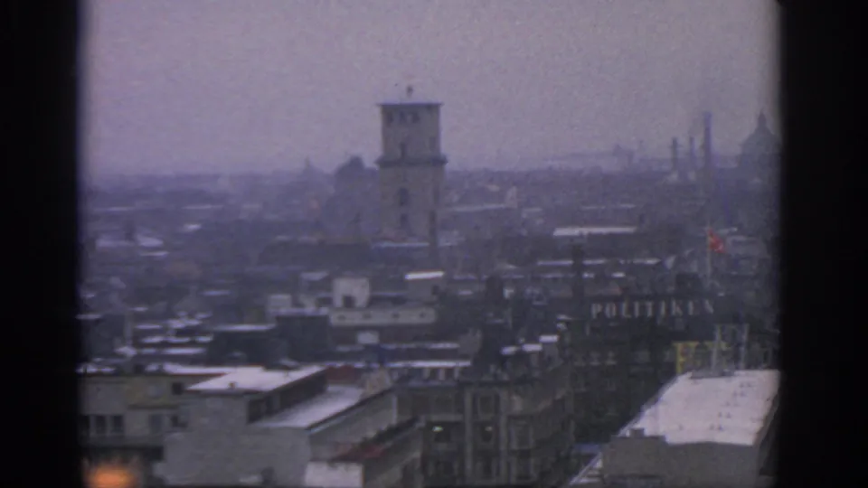 1963 Warsaw view across snow-dusted rooftops toward a tower, distant spires, and a partly visible POLITIKEN sign in haze.