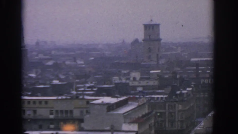 1963 Warsaw skyline seen through haze, with snow on flat roofs, a prominent tower, and partial POLITIKEN lettering at the right edge.